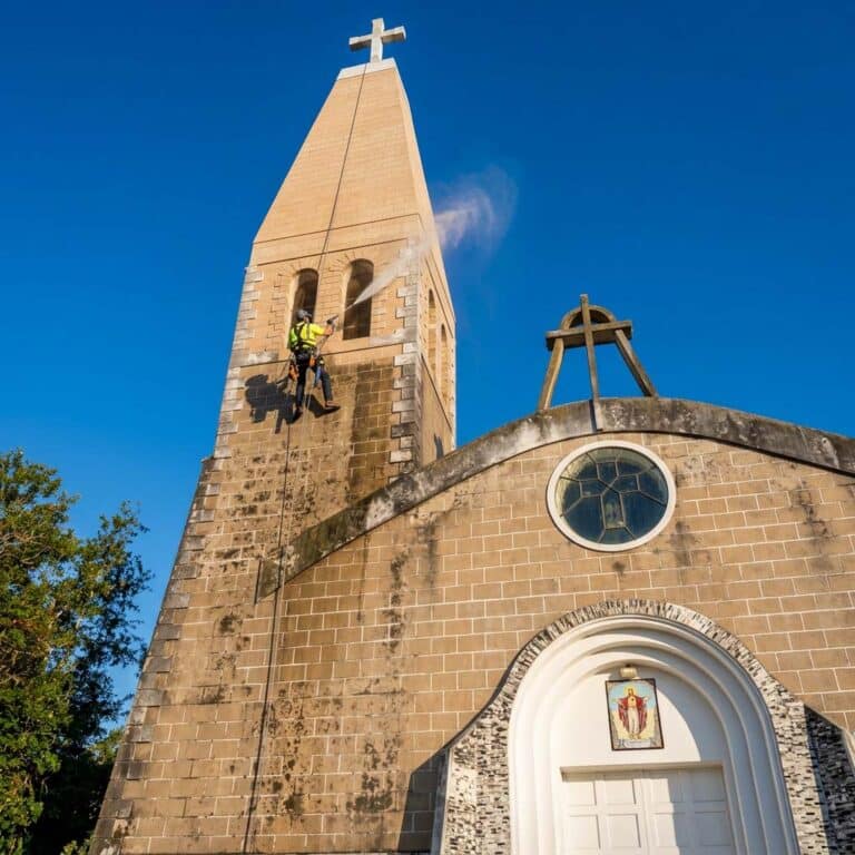 Operario de Limpia Pro realizando hidrolavado de la fachada de una iglesia con acceso por cuerdas